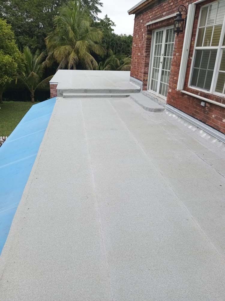 A high-angle view of a newly installed, light-gray flat roof on a building with a red brick exterior and white windows.