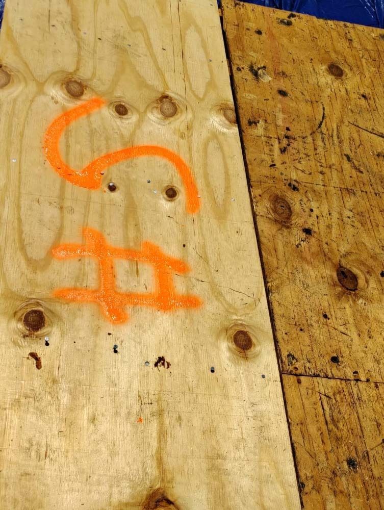 Two pieces of plywood side-by-side, the left one marked with bright orange spray paint of a 