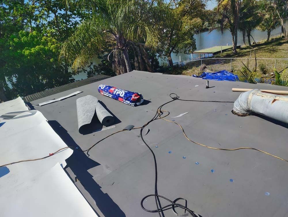 A rooftop under construction with rolls of black roofing material, tools, and a white ventilation pipe.
