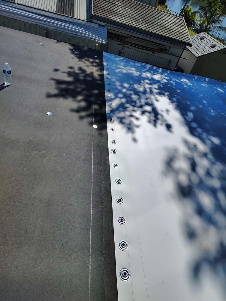 A view of a roof showing a seam where a dark gray membrane meets a light-colored membrane secured with a line of fasteners.