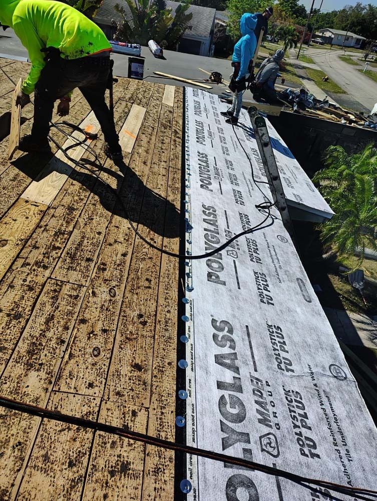 Two workers in high-visibility and blue clothing install Polyglass underlayment on a residential roof.