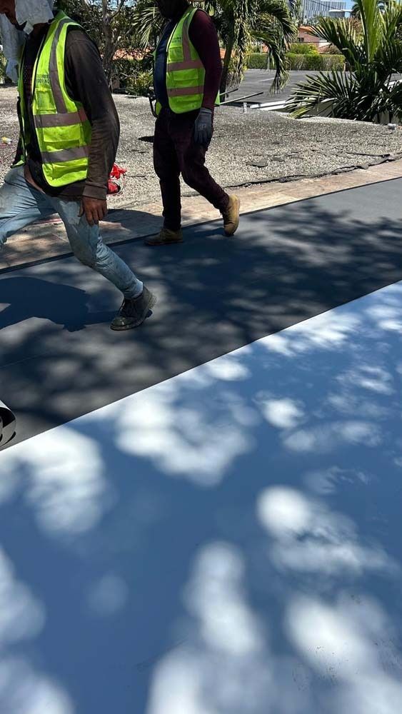 Two workers in high-visibility vests walk across a partially painted white surface outdoors.