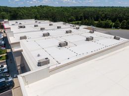 An aerial view of a white flat commercial roof with multiple HVAC units and a parking lot to the left.