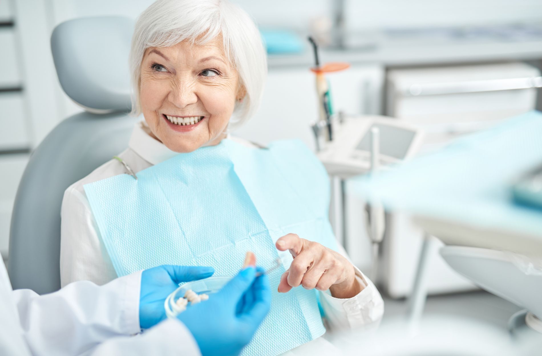 An elderly woman is smiling while sitting in a dental chair.