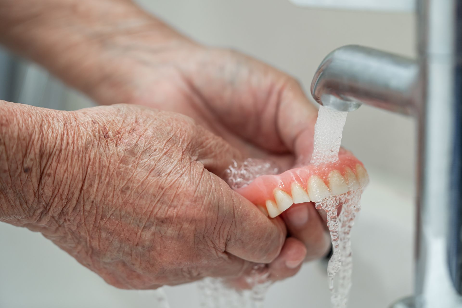 an elderly man is washing his dentures in a sink.