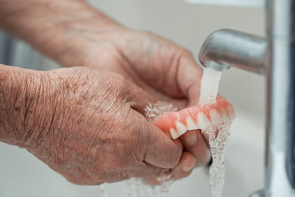 pair of hands washing snap-on dentures under running water.