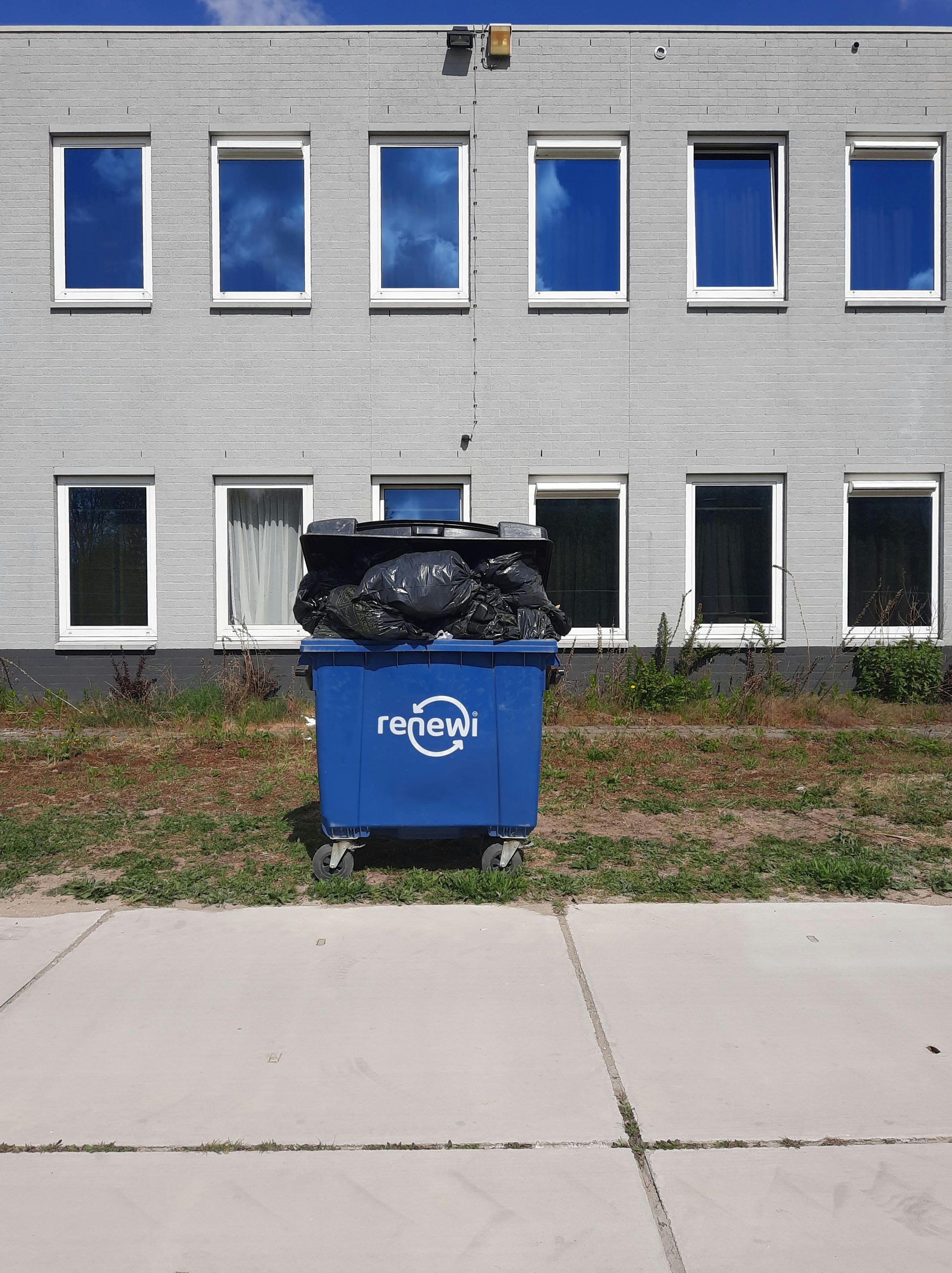 A blue recycling bin is sitting in front of a building