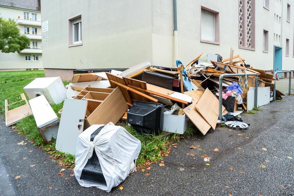 Pile of discarded furniture and debris on a sidewalk next to an apartment building.