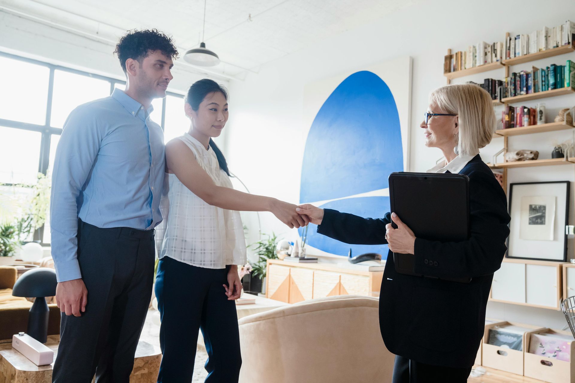 Couple shaking hands with realtor in a brightly lit room; agreement, handshake.