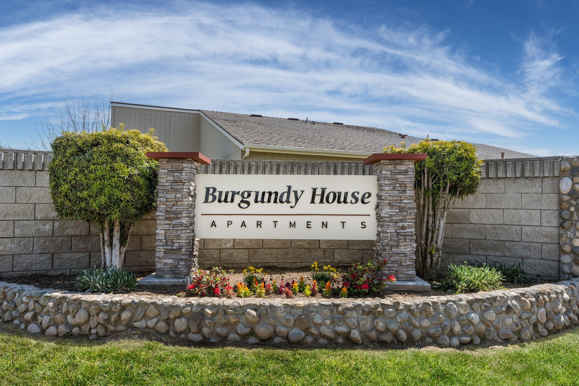Sign for Burgundy House Apartments with a brick and stone facade, with a sunny blue sky.