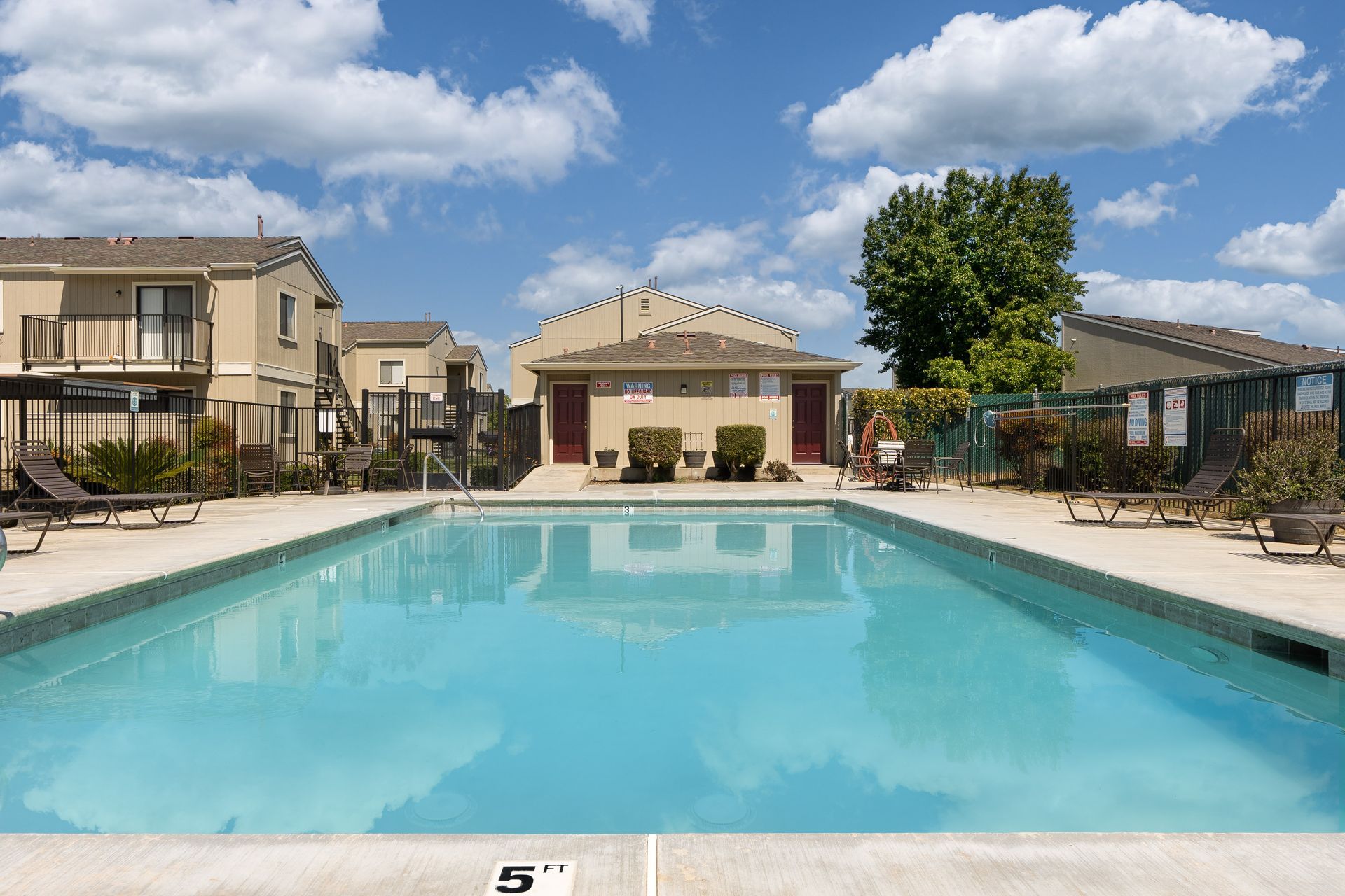 Swimming pool in front of apartment buildings on a sunny day with lounge chairs.