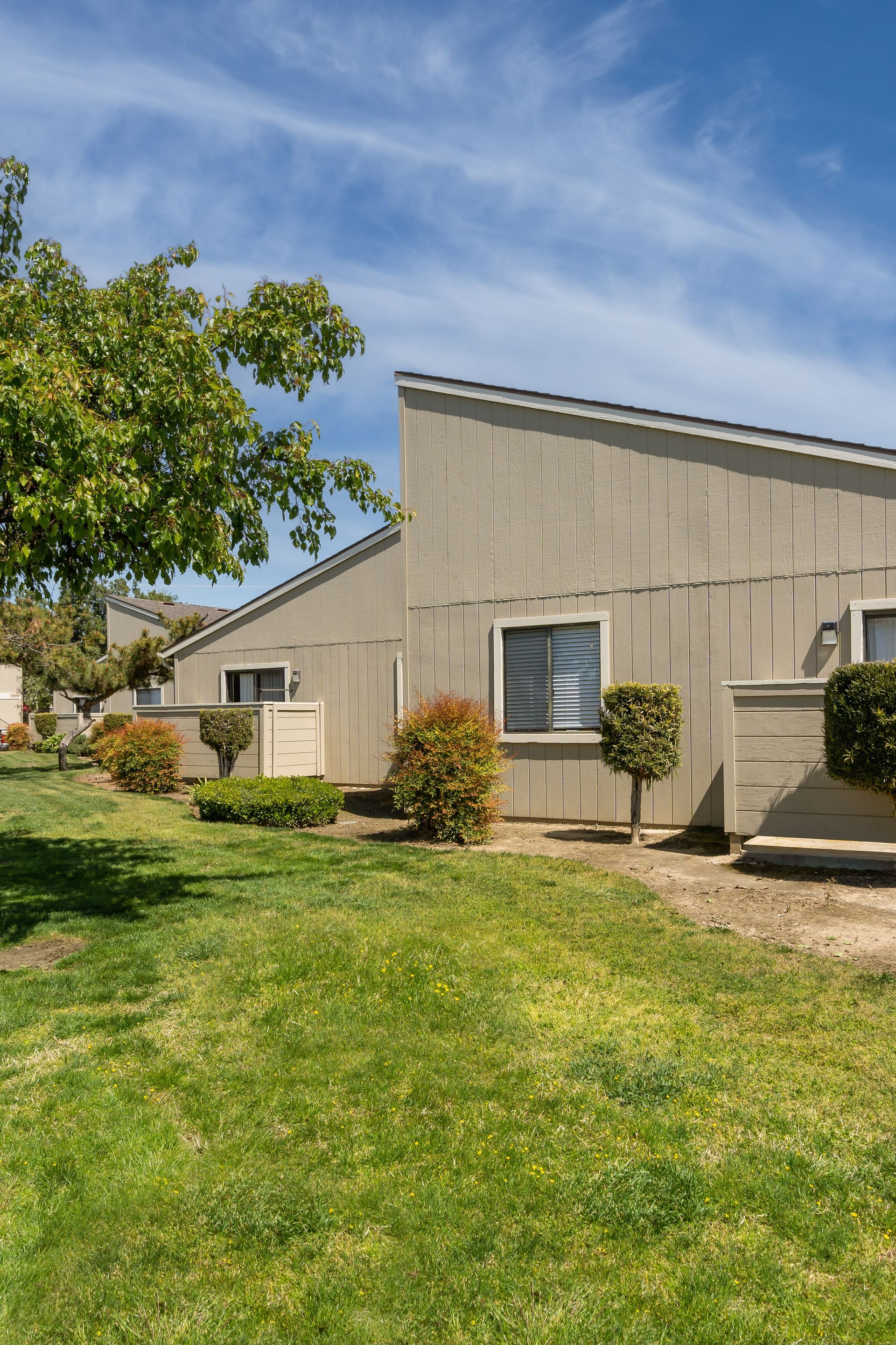 Townhomes with light beige siding, green lawn, and blue sky.