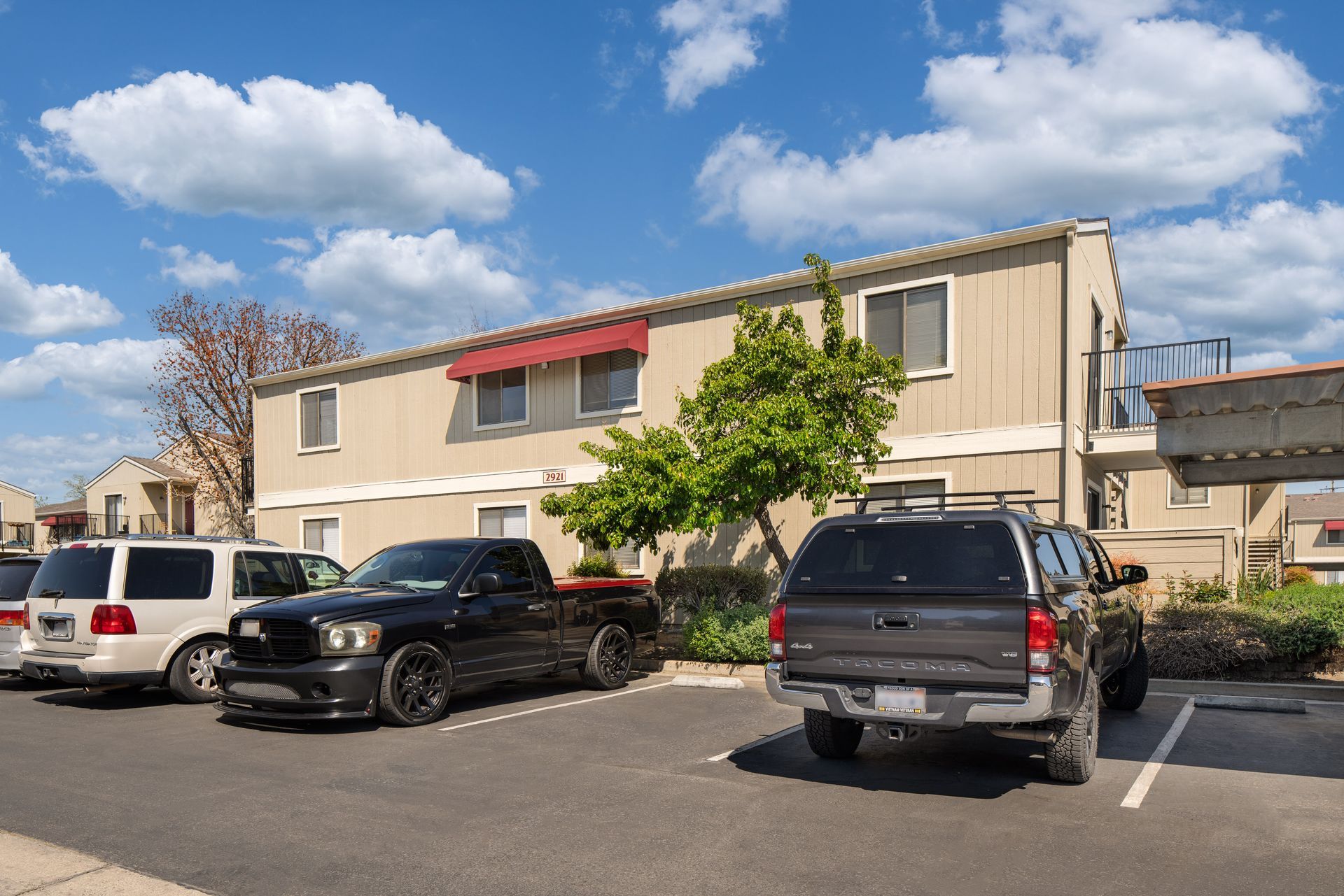 Apartment complex with parked cars under a bright blue sky with puffy clouds.