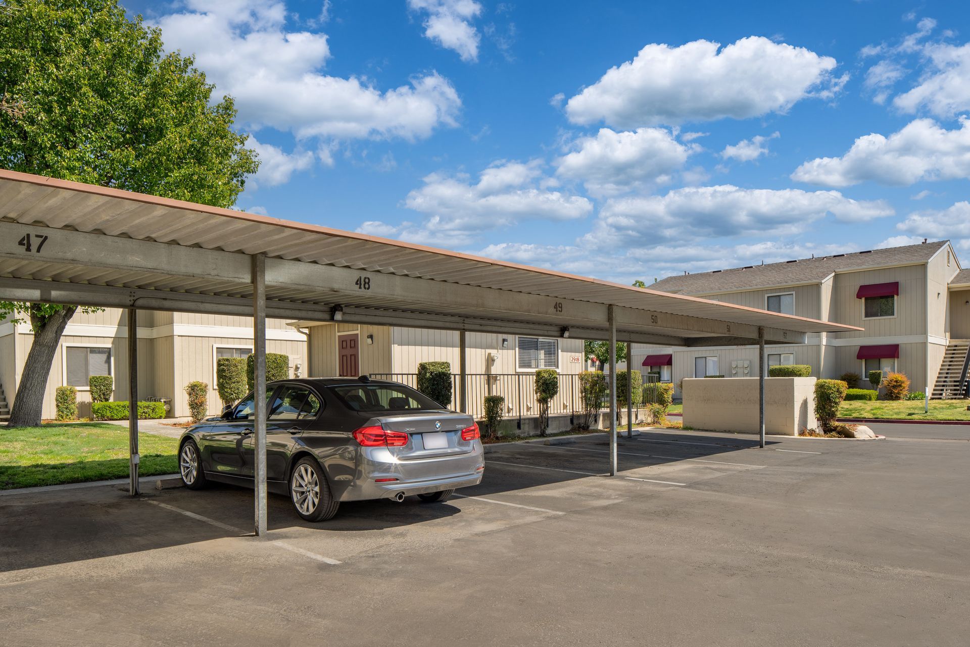 Car parked under a carport in front of apartment buildings on a sunny day.