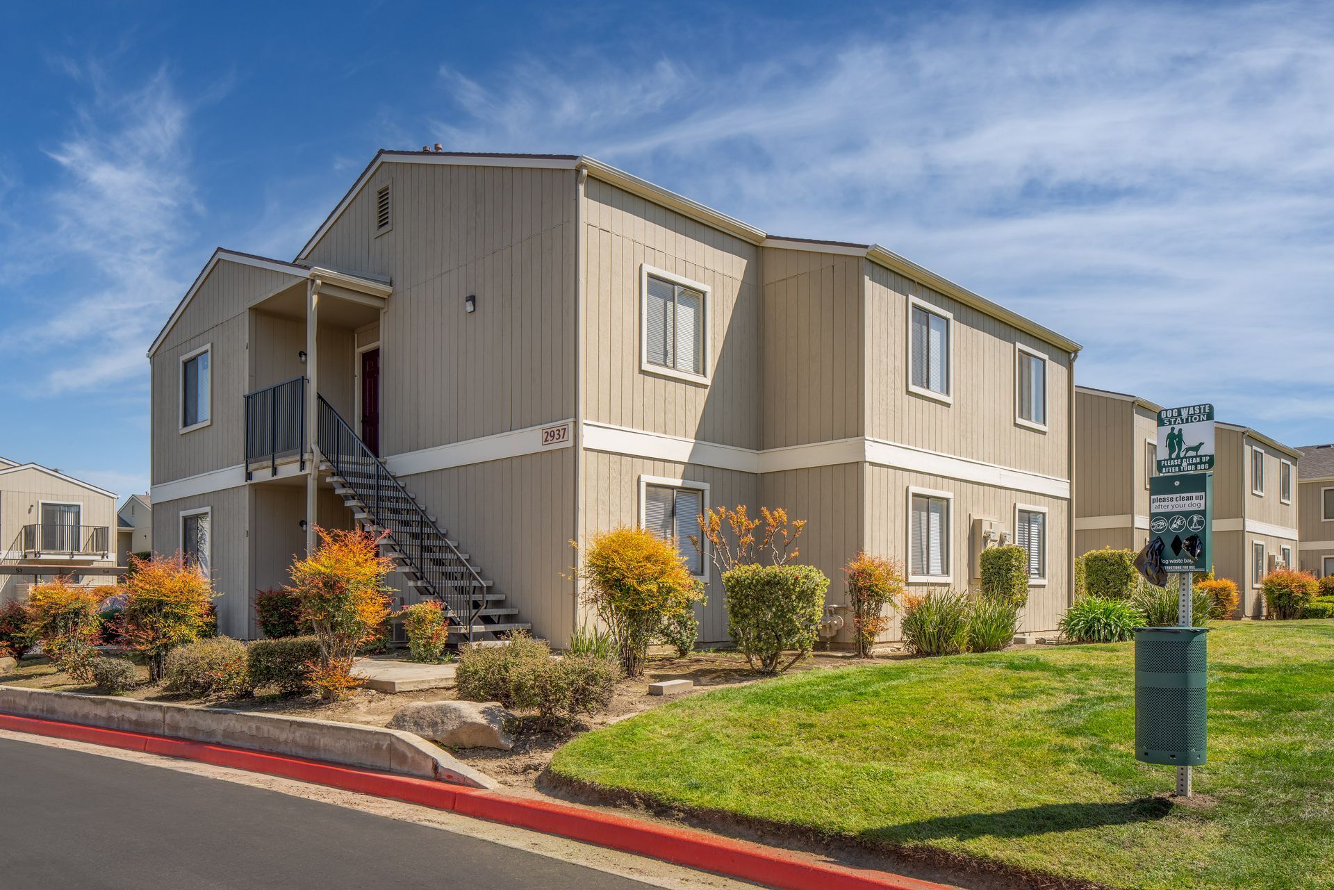Apartment building, tan with green grass, red curb, blue sky.