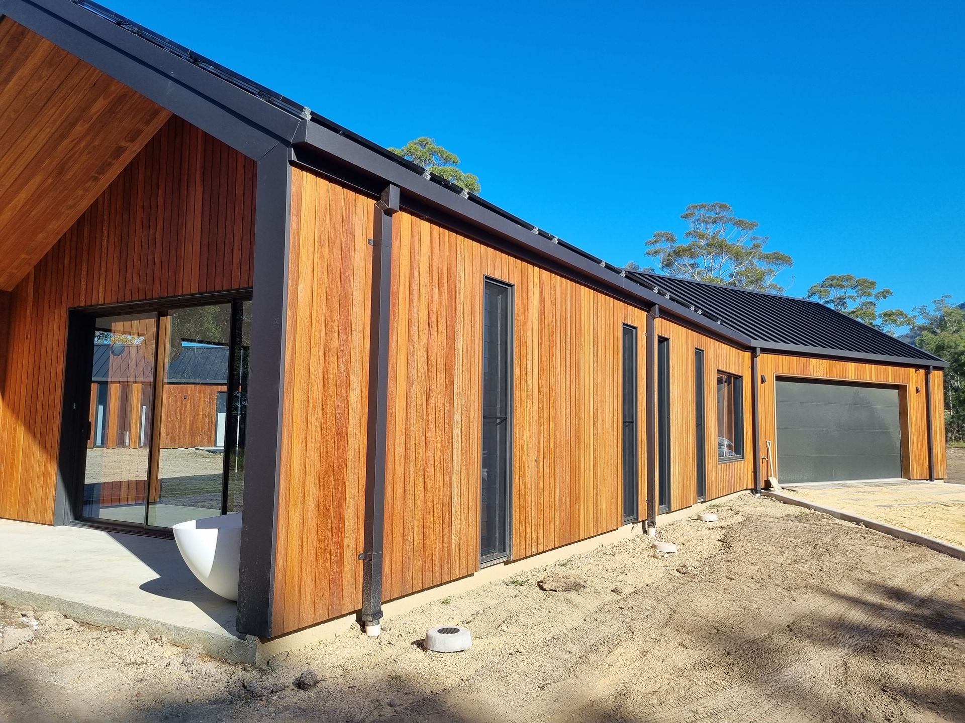 Wooden-clad modern house with dark trim and garage on a sunny day.