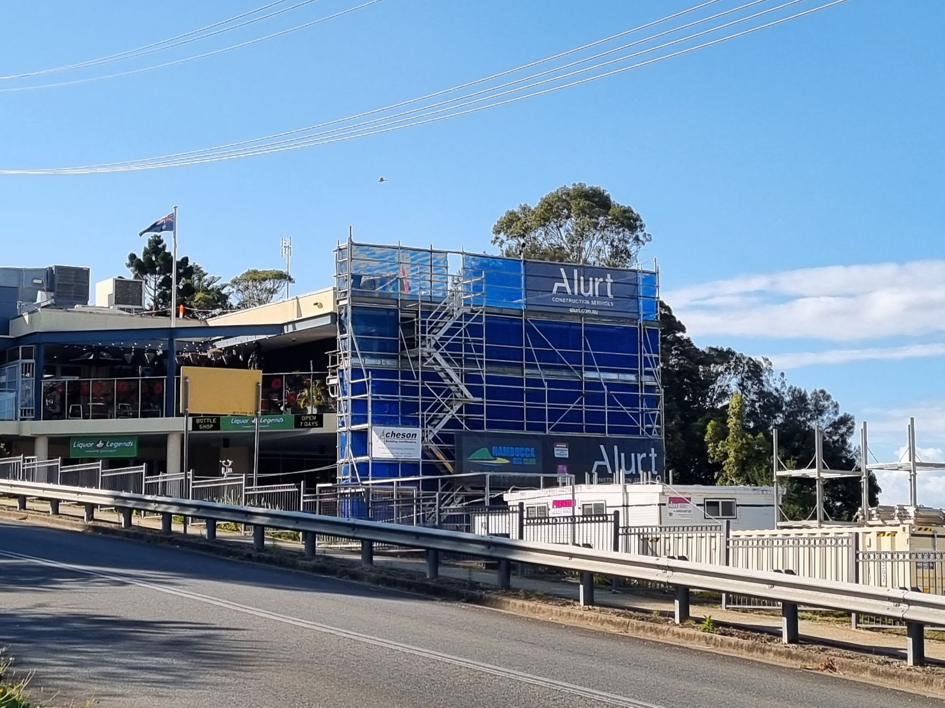 Building under construction, scaffolding wraps a facade. Blue tarp, road, sky, and power lines.