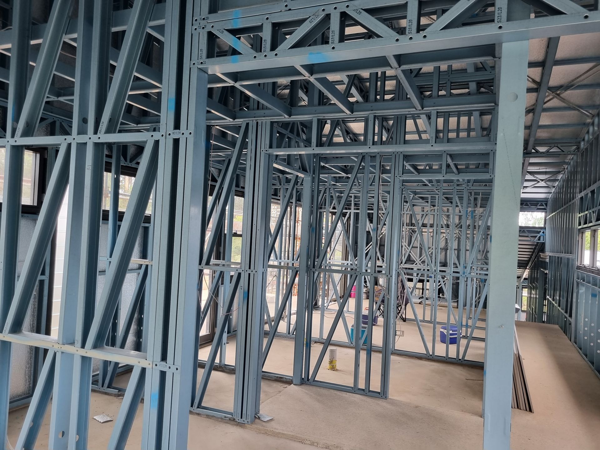 Blue steel framing of a building's interior under construction, showing walls, doorways, and ceiling supports.