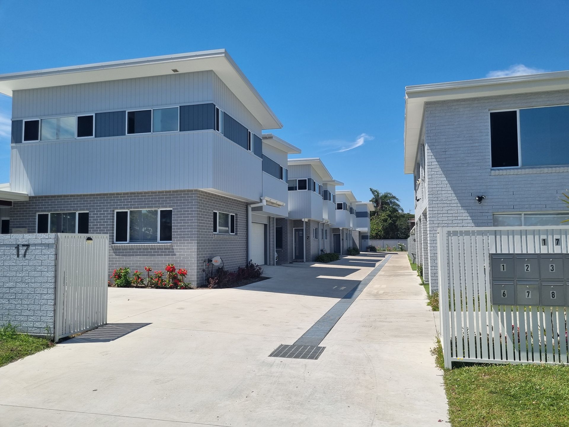 Row of light gray, two-story townhouses with a concrete walkway and blue sky.