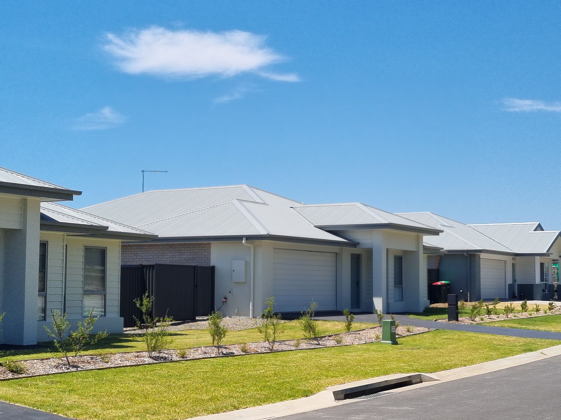 Row of modern, single-story houses with gray roofs and white exteriors on a sunny day.