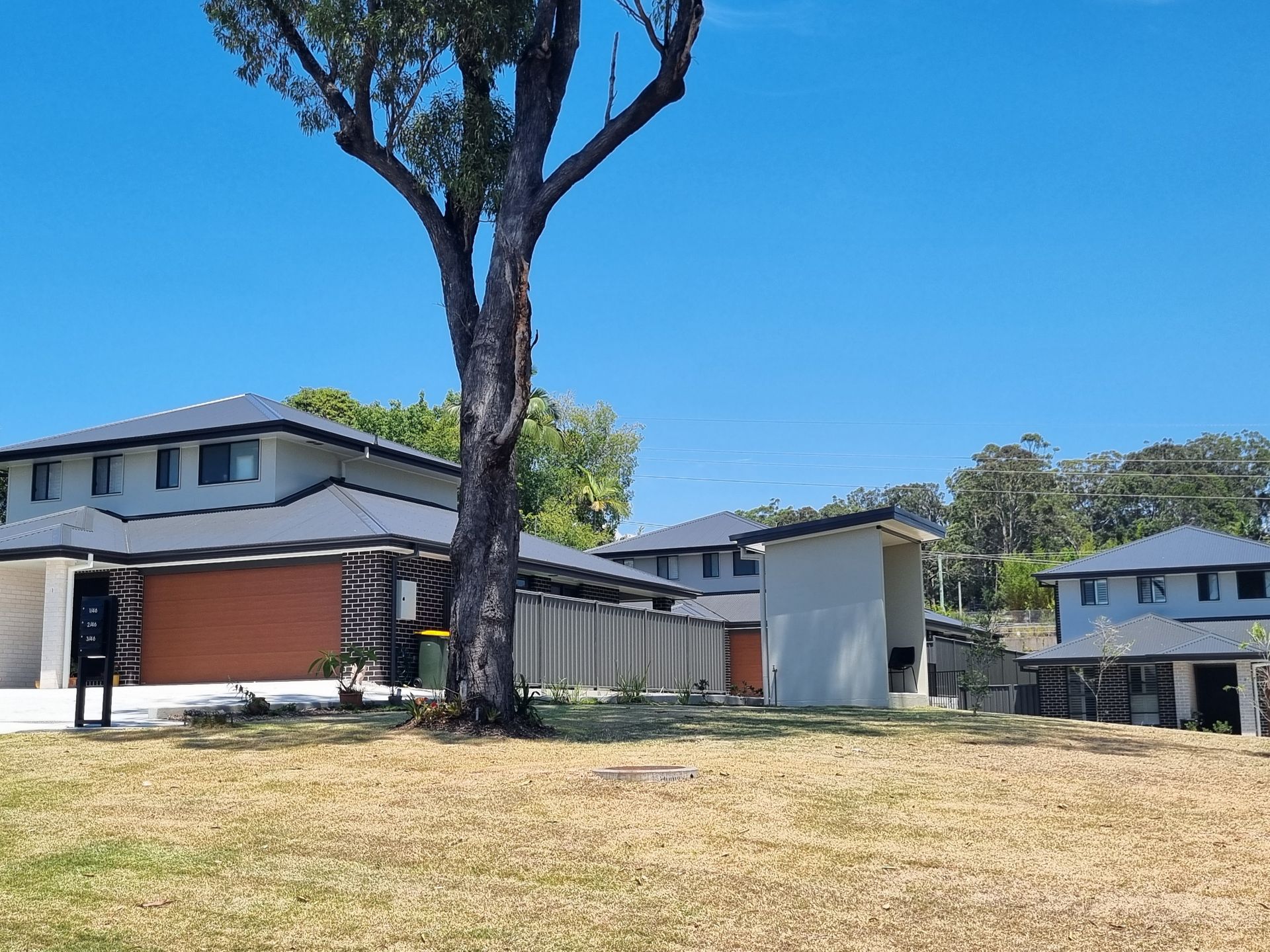 Houses with gray roofs, brown garage doors, and a tree in front. Blue sky.