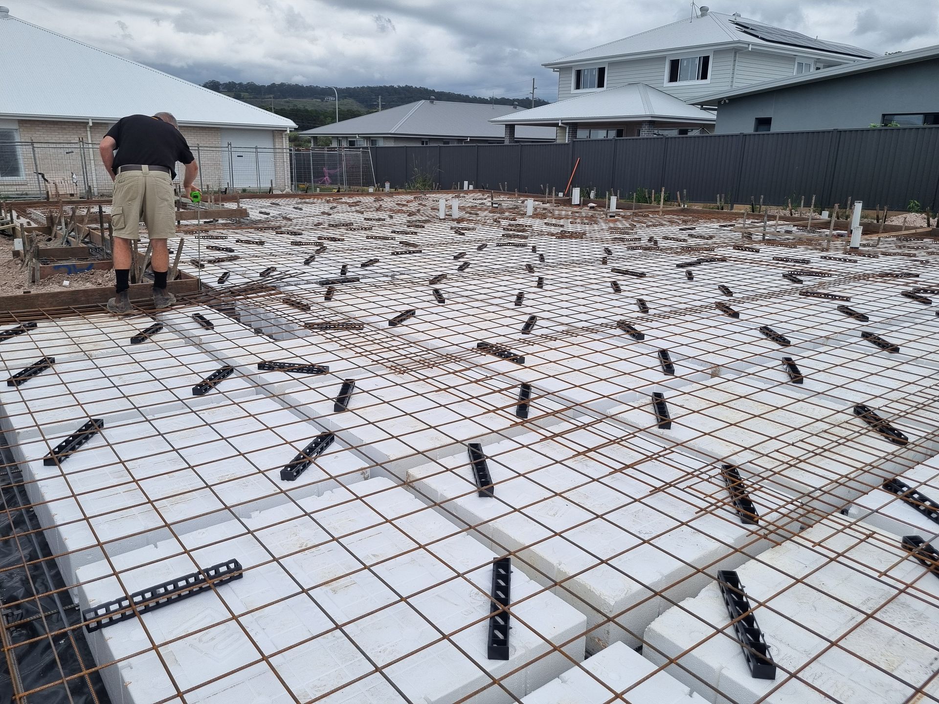 Construction site with worker: Styrofoam blocks, rebar grid, black clips, preparing for concrete foundation.