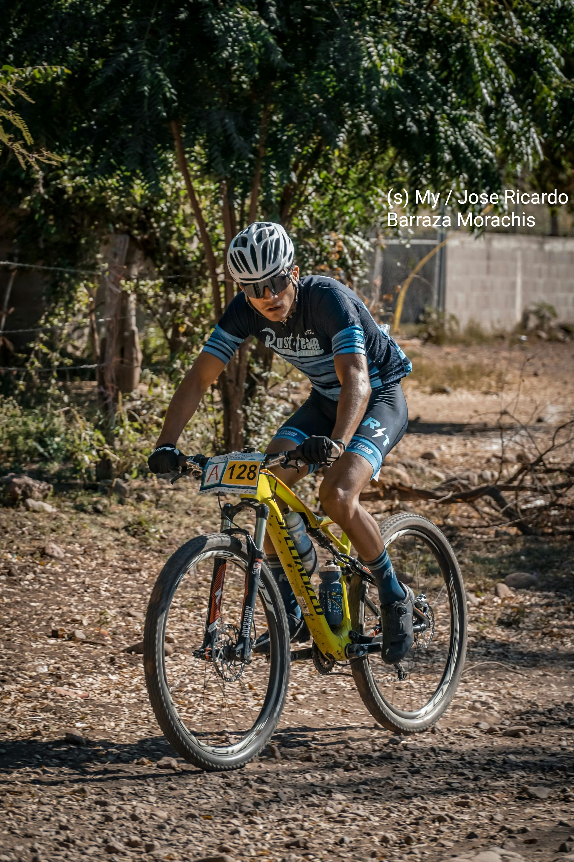 Cycliste roulant sur un vélo jaune sur un chemin de terre, portant un casque et un maillot bleu.