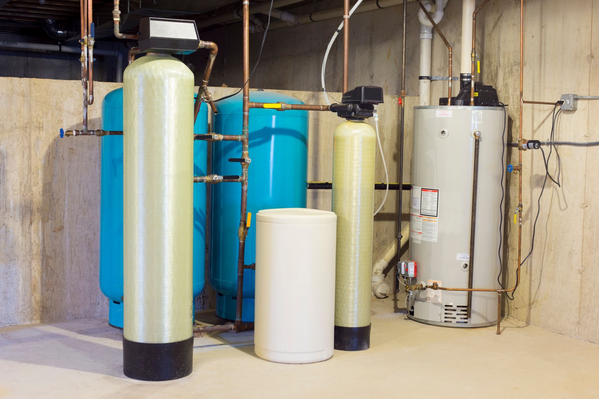A row of water tanks and a water heater in a basement.