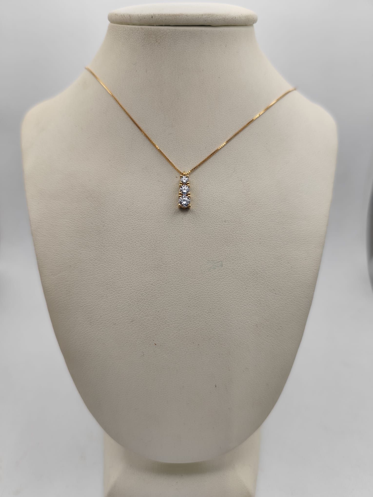 Collana in oro con tre piccole pietre trasparenti su un manichino beige.