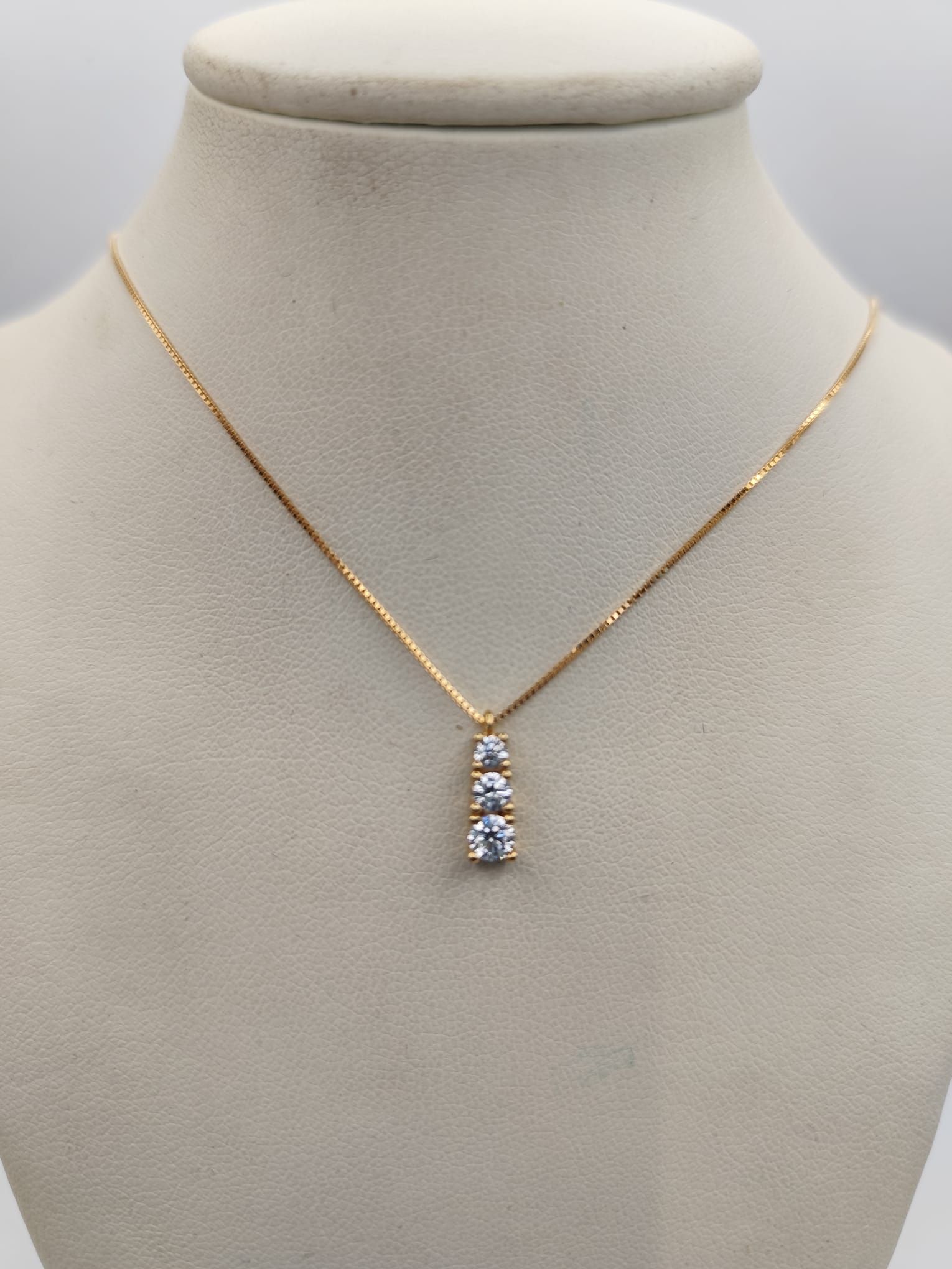 Collana in oro con tre pietre bianche scintillanti appese a una catena su un manichino color cuoio.