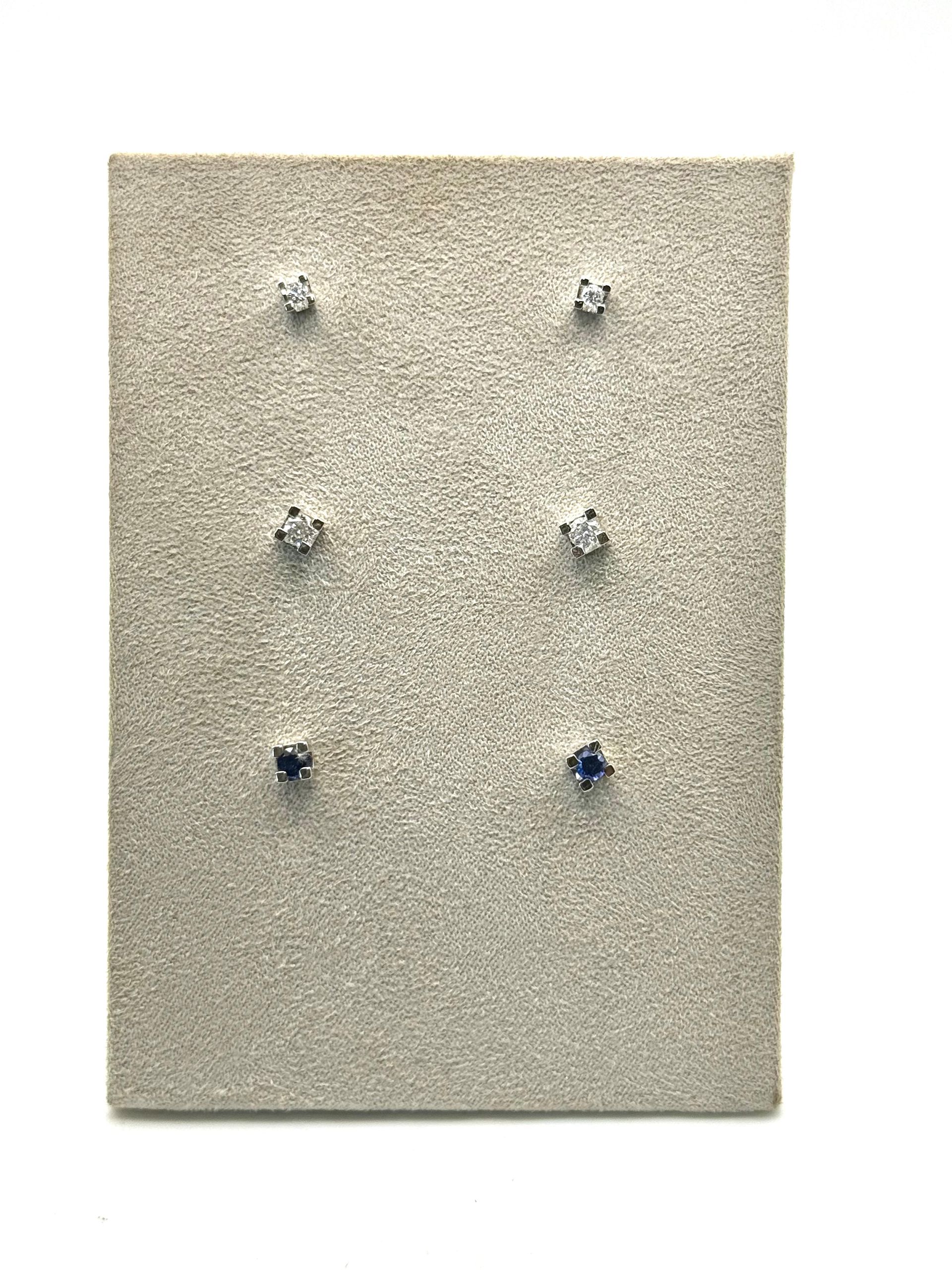 Orecchini a bottone con smeraldi esposti su un portagioie bianco all'interno di una scatola di legno.