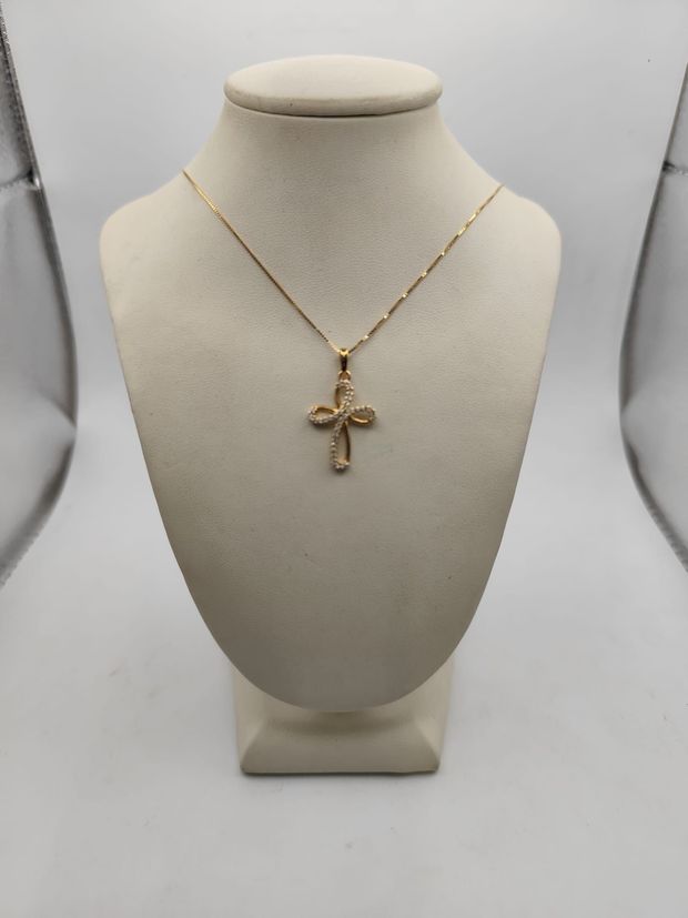 Collana con pendente a croce in oro esposta su un busto color crema su uno sfondo bianco.