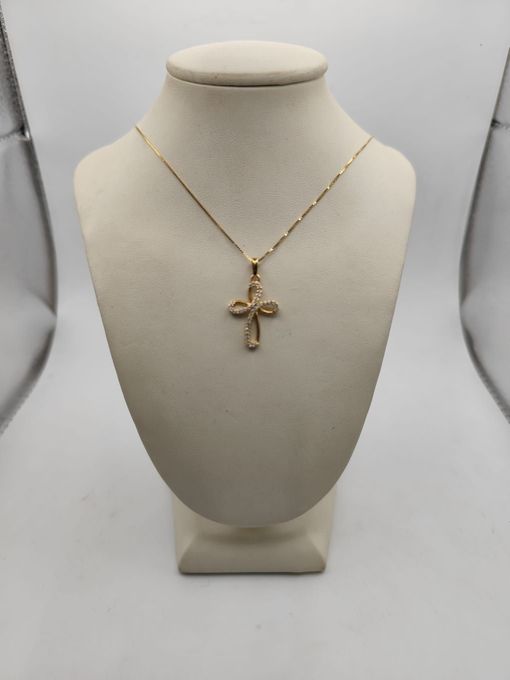 Collana con pendente a croce in oro esposta su un busto color crema su uno sfondo bianco.