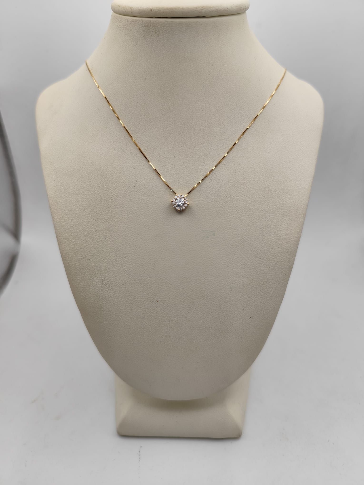 Collana in oro con pendente di diamanti su un busto beige su sfondo bianco.