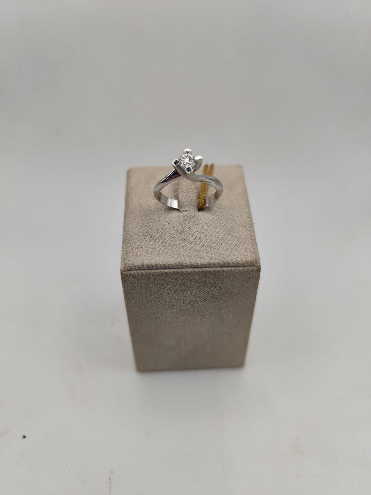 Anello di fidanzamento con diamante su un espositore beige su sfondo bianco.