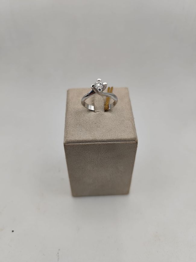 Anello di fidanzamento con diamante su un espositore beige su sfondo bianco.