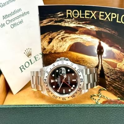 Orologio Rolex Explorer II con quadrante nero, cinturino in acciaio e documenti in una scatola verde.