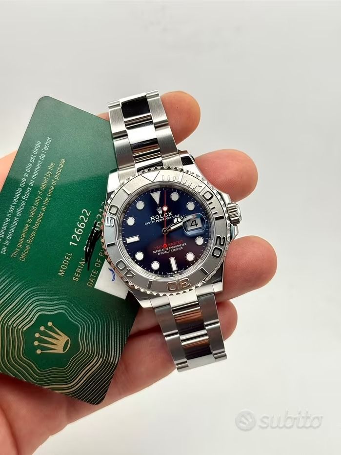 Una persona che tiene in mano un orologio Rolex Yacht-Master in argento con quadrante blu e una carta di garanzia verde.