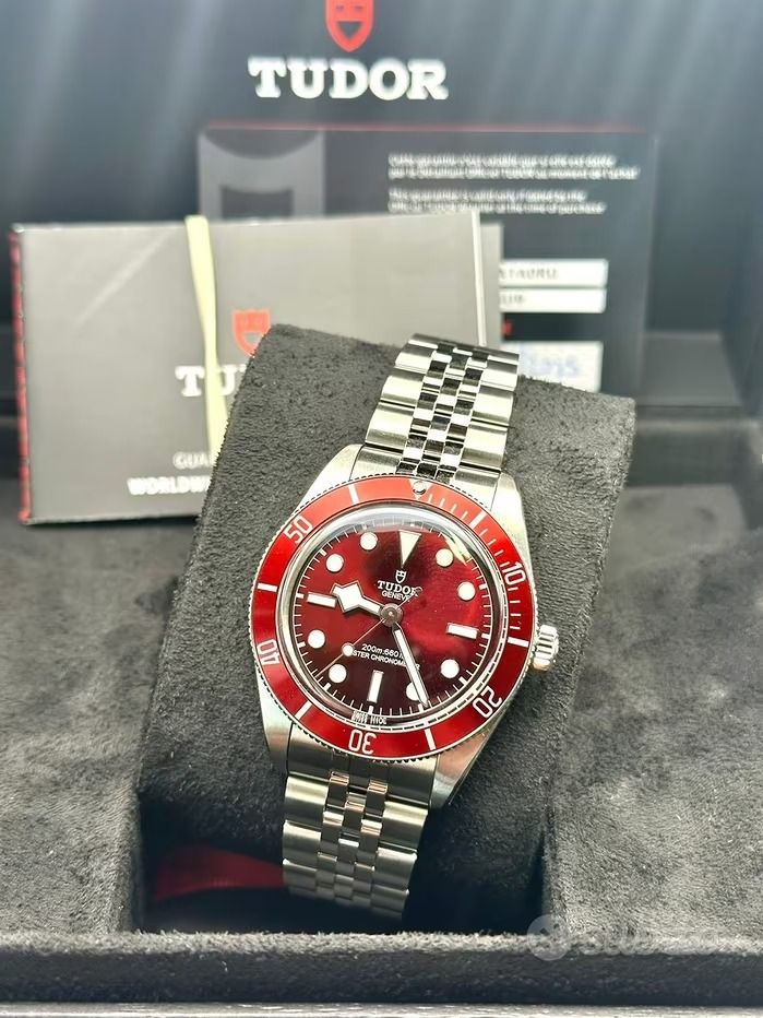 Orologio Tudor Black Bay con lunetta e quadrante rossi su bracciale in acciaio inossidabile, presentato in una scatola.