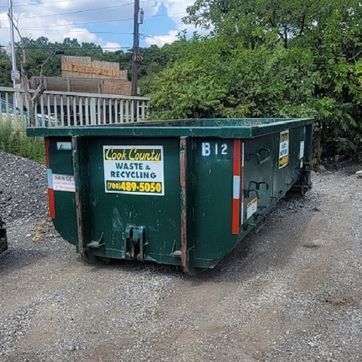 Green dumpster at construction site, with houses in the background.