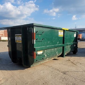 Green dumpster on asphalt, outdoors under a blue sky with clouds.
