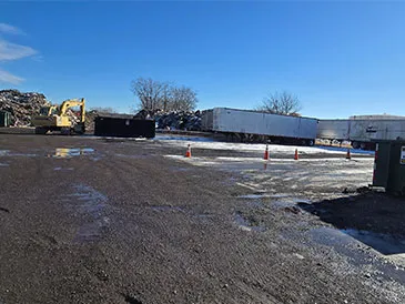Exterior view of a recycling facility on a sunny day. Trucks, machinery, and waste are visible.