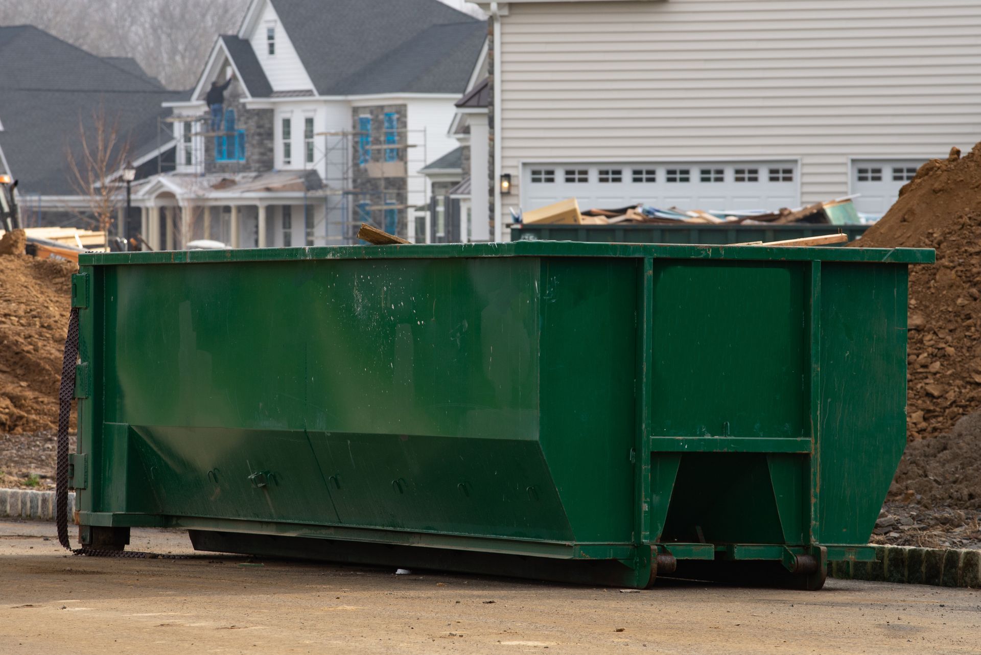 Green dumpster at construction site, with houses in the background.