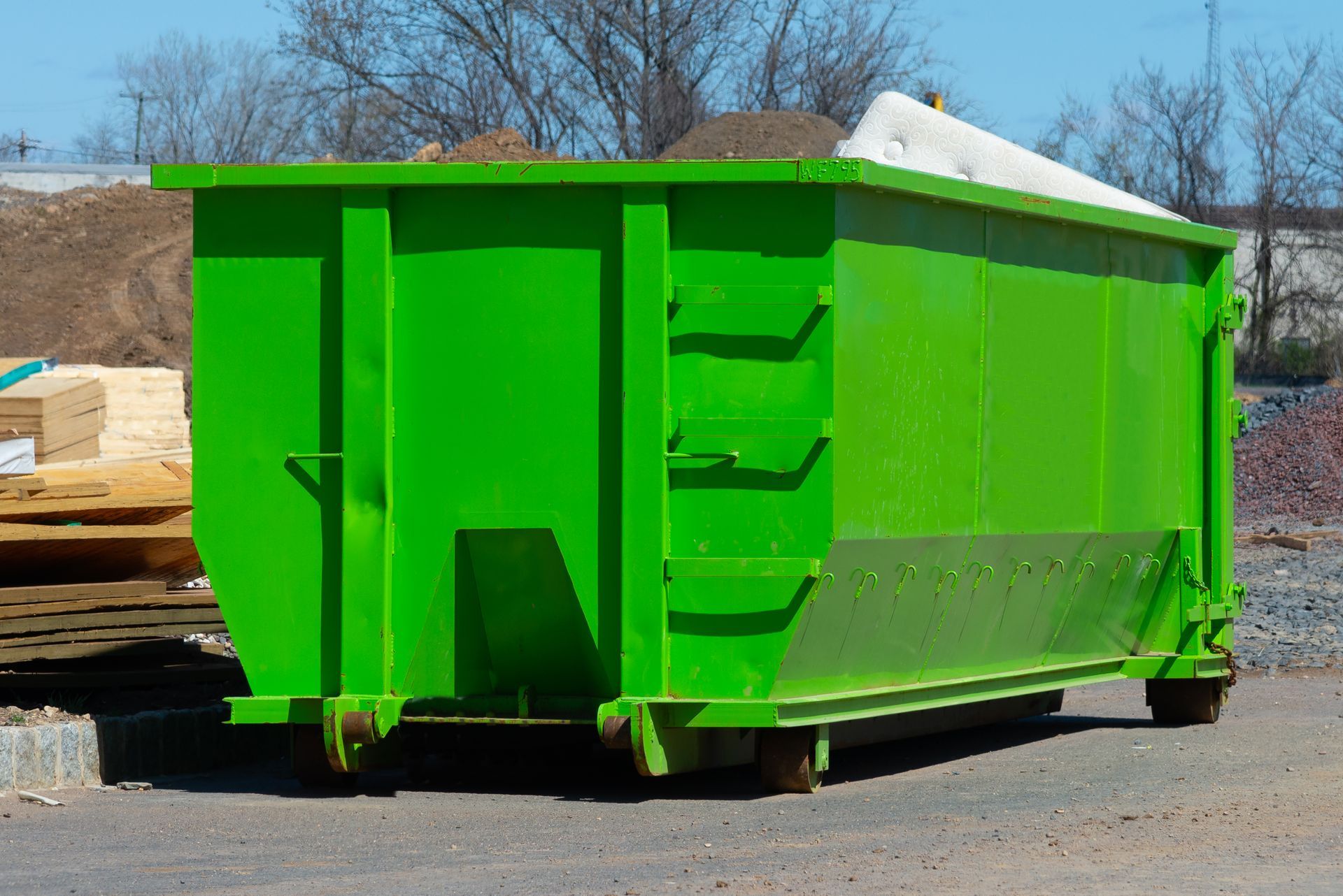 Bright green dumpster on wheels, outdoors near building materials.