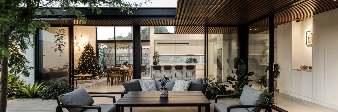 Outdoor patio with black table and chairs, looking into a modern home with dining and kitchen areas.