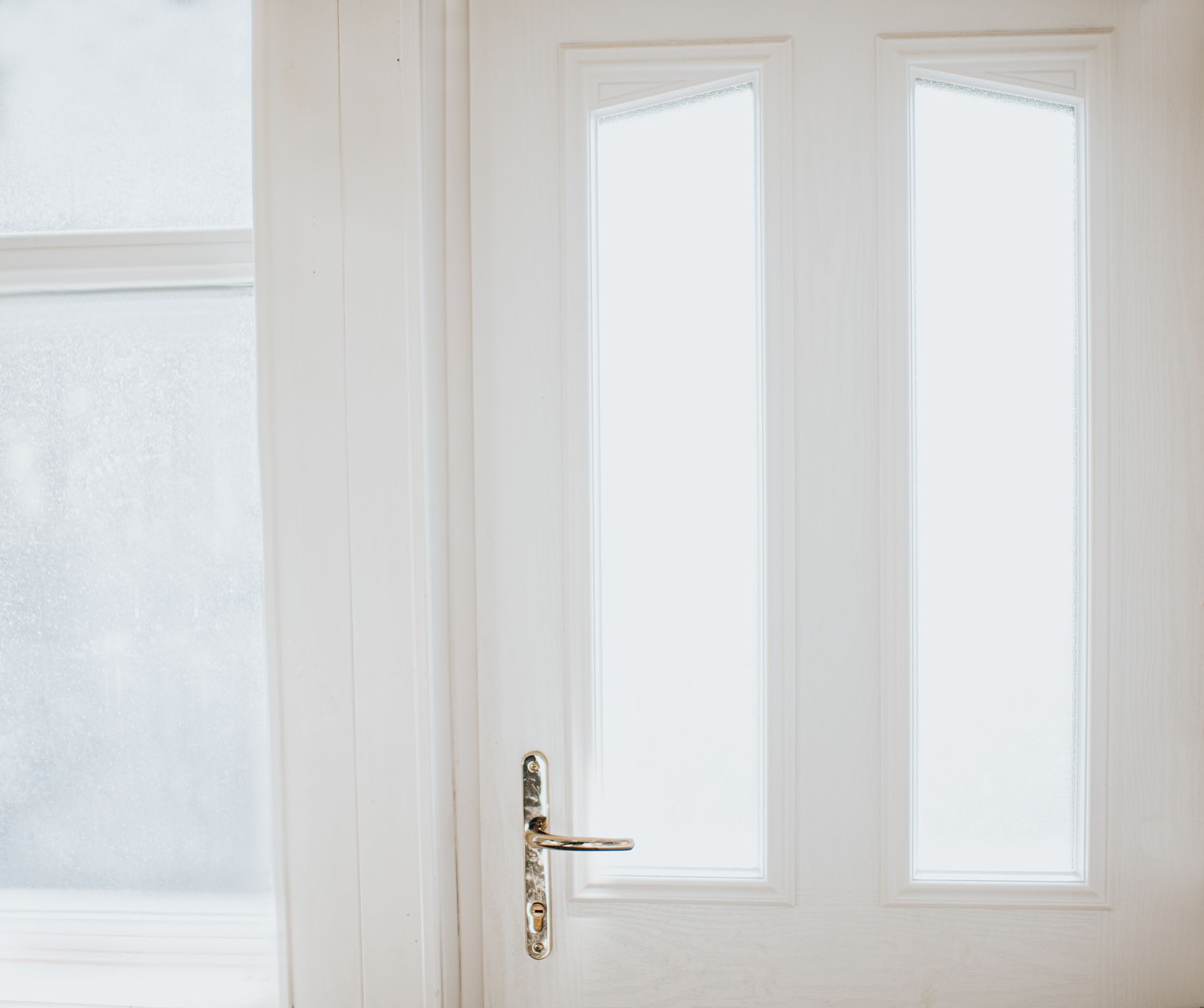 A white door with two frosted glass panels and a silver handle next to a frosted window frame A white door with two frosted glass panels and a silver handle next to a frosted window frame