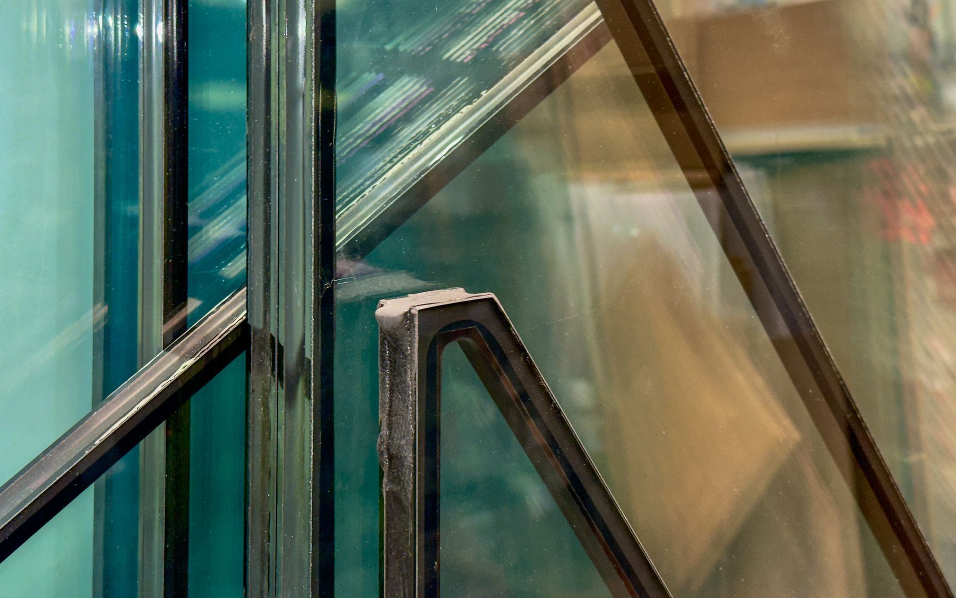 Close-up of layered glass panels with black frames, possibly for a window or door, reflecting light and blurry interior views.