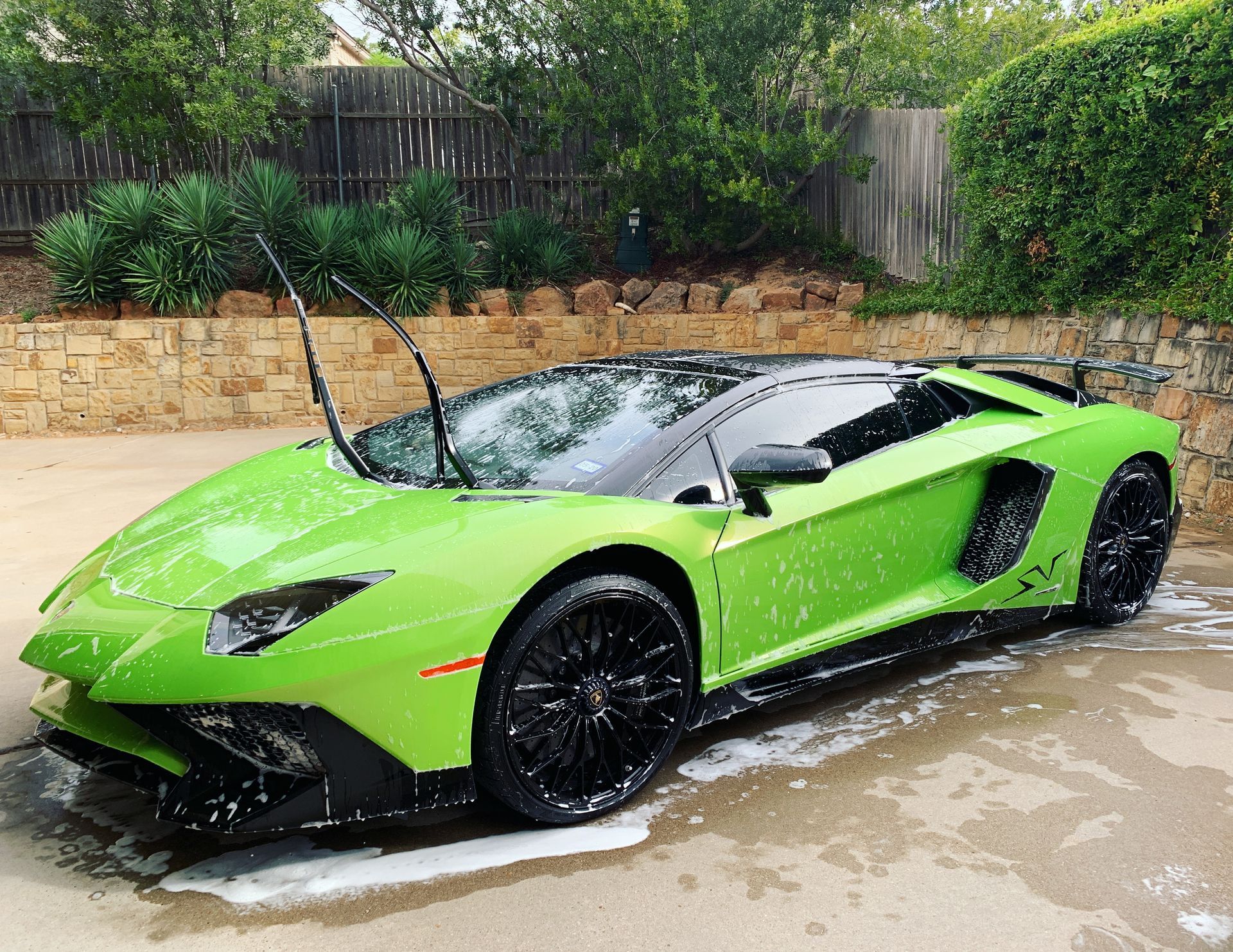 Green Lamborghini being washed with soapy water in a driveway.