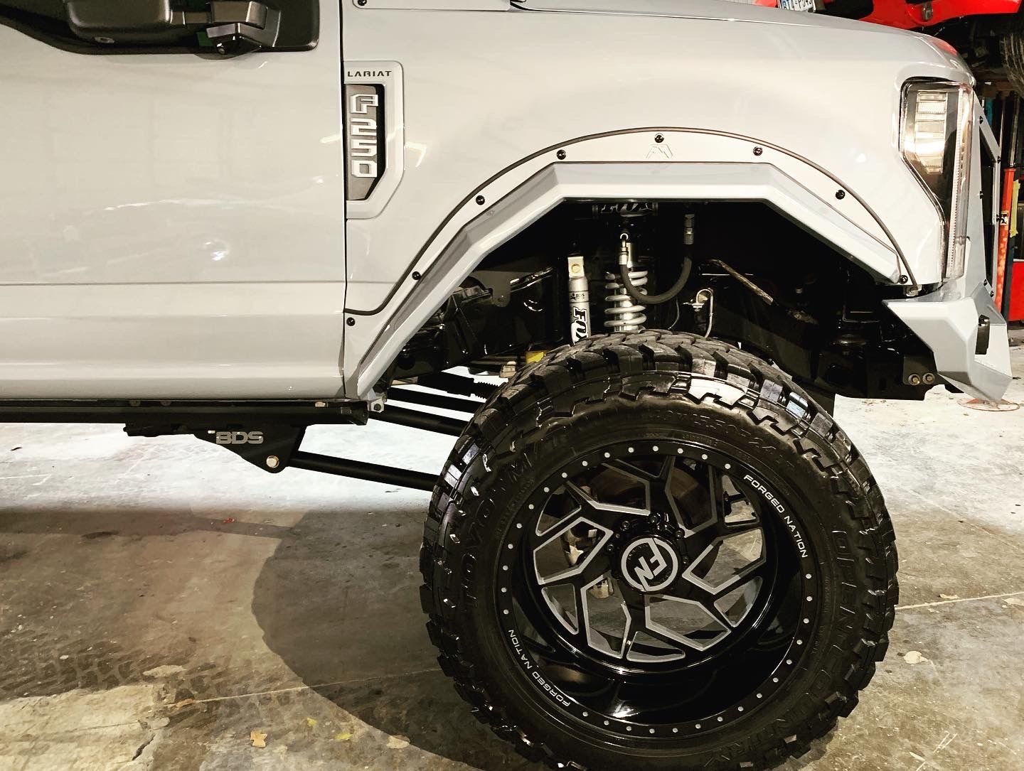 Grey lifted truck with large black wheels, modified fenders, and a side view.