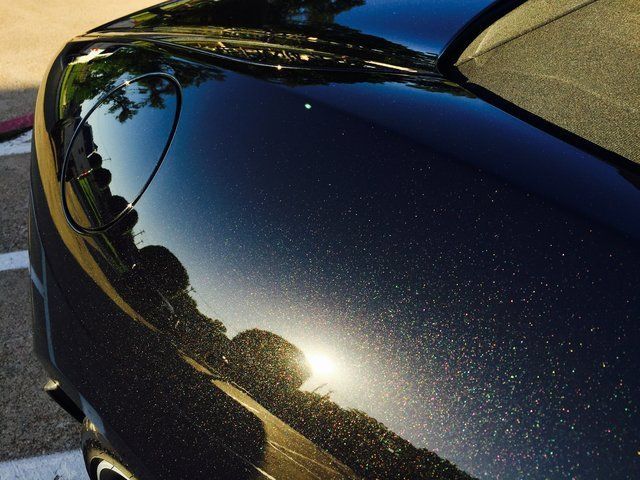 Black car hood reflecting a sunny outdoor scene with visible sparkles.